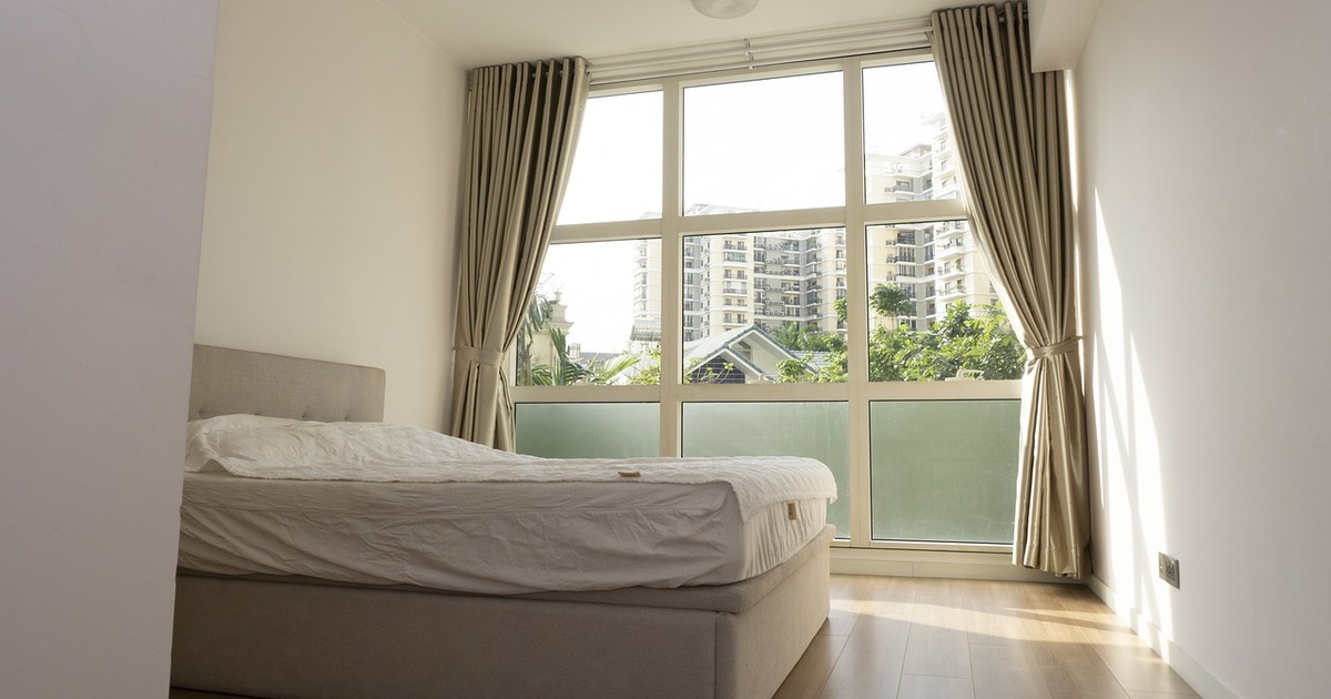 A bedroom with a bed, open windows, and light bedroom wall colours.