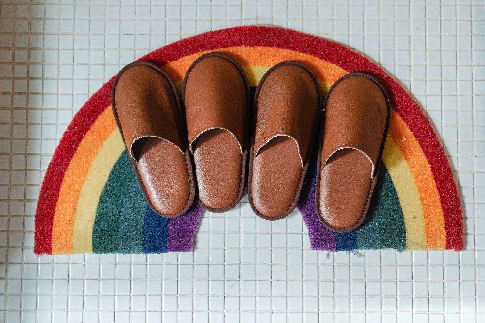 Two pairs of brown slippers on a rainbow bath mat.