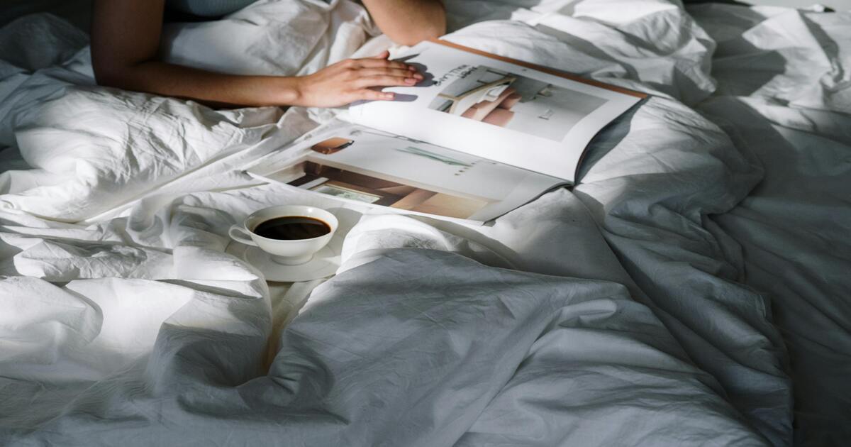 A person in a guest bedroom drinking coffee in bed.