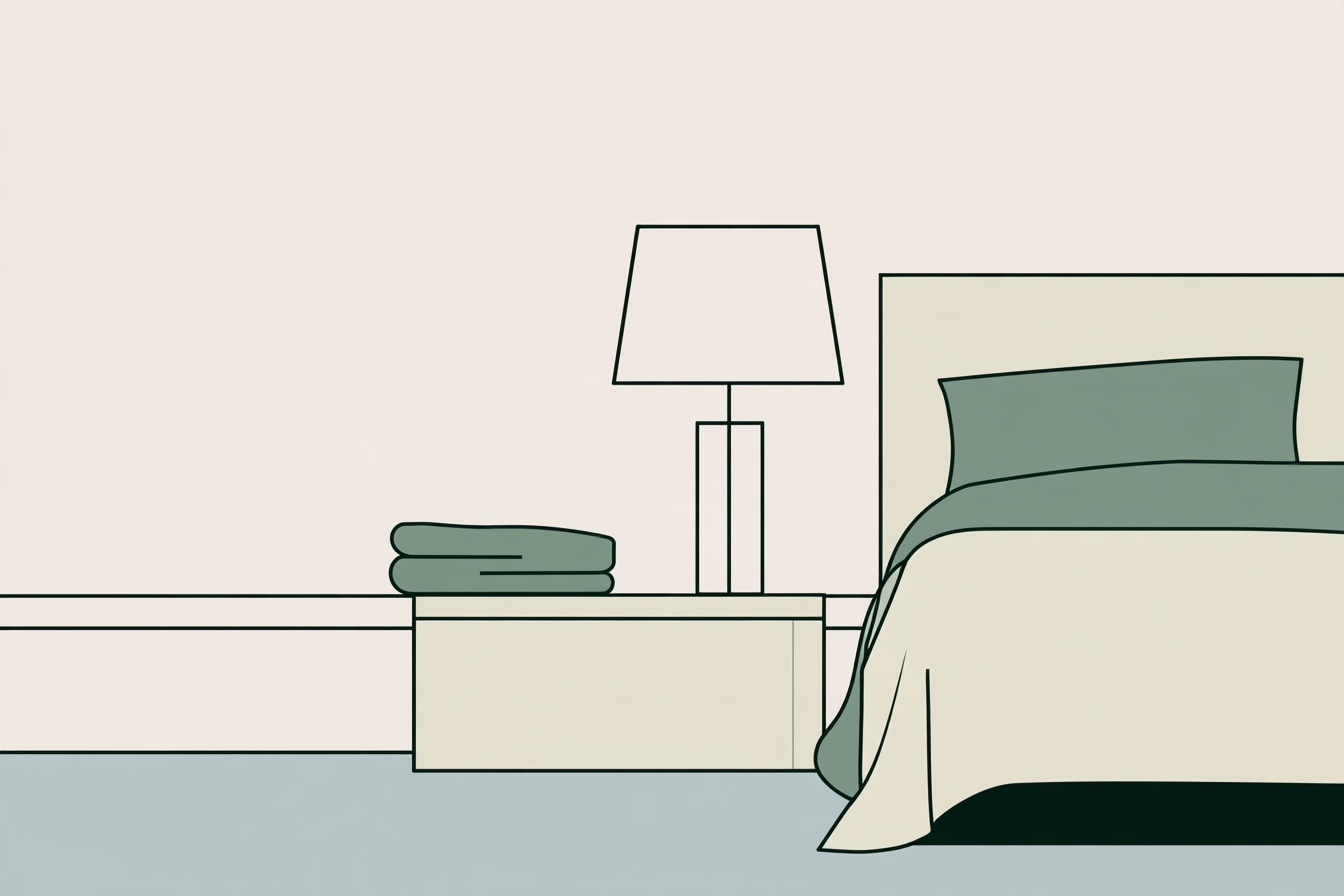 A simple bedside cabinet with a lamp and folded textile beside a neatly made bed.