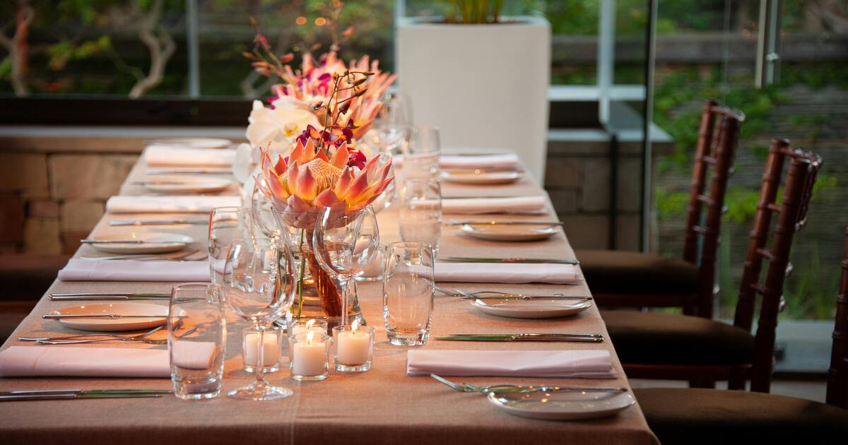 A table set with white plates, beige table linens, and a floral centerpiece.